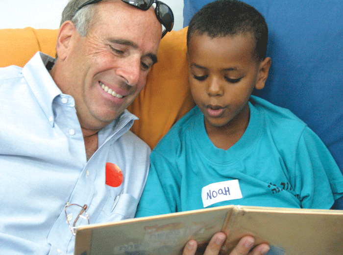 Minnetonka resident Bruce Goldstein, who has hosted PACT Hadera participants, listens as Noah, a student in PACT’s Alternative Learning Space program in the Givat Olga school, reads a Hebrew book about a dog and a cat. (Photo: Mordecai Specktor)