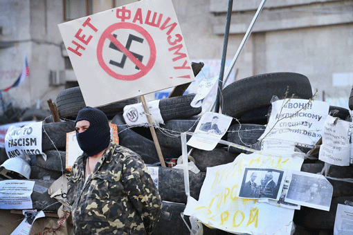 A pro-Russian activist guards the front of the Donetsk Regional Administration building on Friday, in Donetsk, Ukraine. The activists occupying the building have surrounded it with a barricade of tires and barbed wire, and have a cache of Molotov cocktails strategically placed within the barricade. The sign with the crossed out swastika reads "No to fascism," an allusion to the assertion by pro-Russian groups that the new Ukrainian government is dominated by fascists. (Photo: Scott Olson/Getty Images)