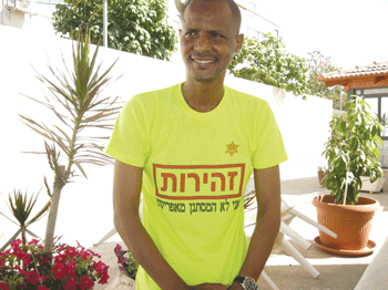 Elias Inbram wears a shirt he made that features a yellow star and reads: “CAUTION — I am not an infiltrator from Africa!” (Photo: JTA)